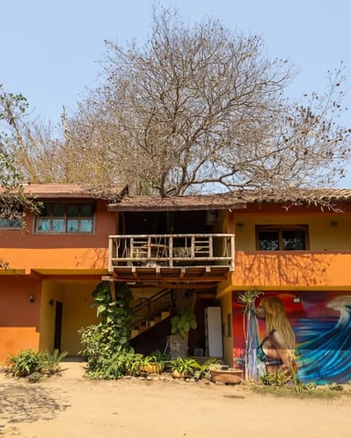 Orange and yellow multi-level beach house with wooden deck, sandy courtyard, and bare trees overhead