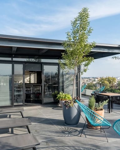 Open-plan living room with gray sofa, dining table, and glass doors opening to balcony with tropical plants