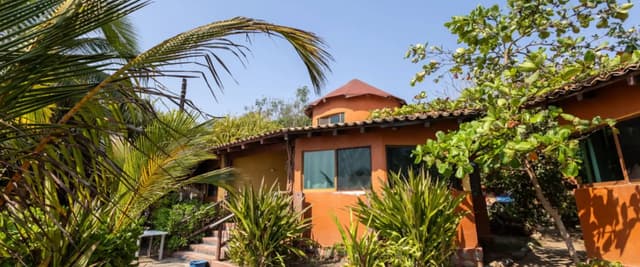 Orange stucco house with curved roof surrounded by palm trees and tropical vegetation